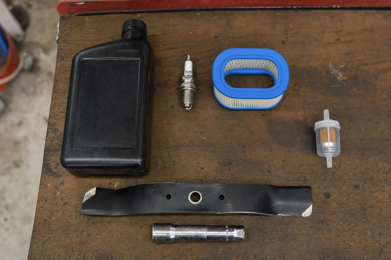 Tune up parts laid out on a workbench: oil, spark plug, air filter and a sharpened blade